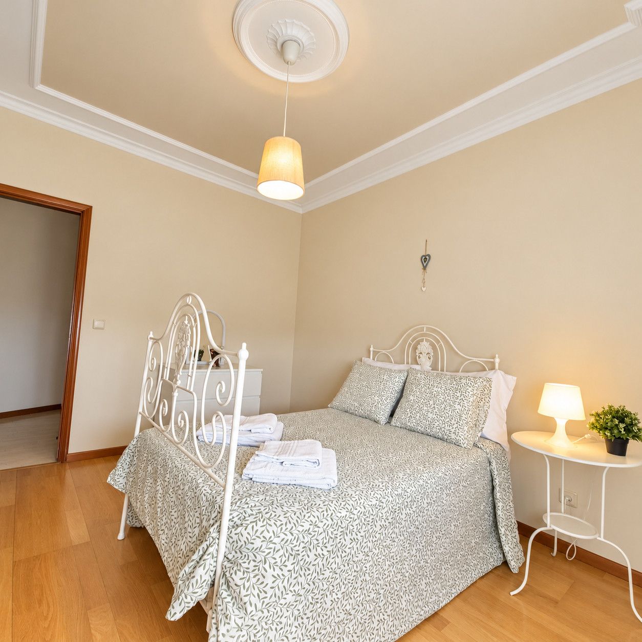 Un dormitorio con cama, mesita de noche, lámpara y una pequeña planta en maceta.