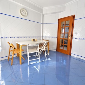 A room with a white tiled wall, a wooden door, a white table with chairs, and a clock on the wall. - Golegã Central by Gthouse (Golegã)