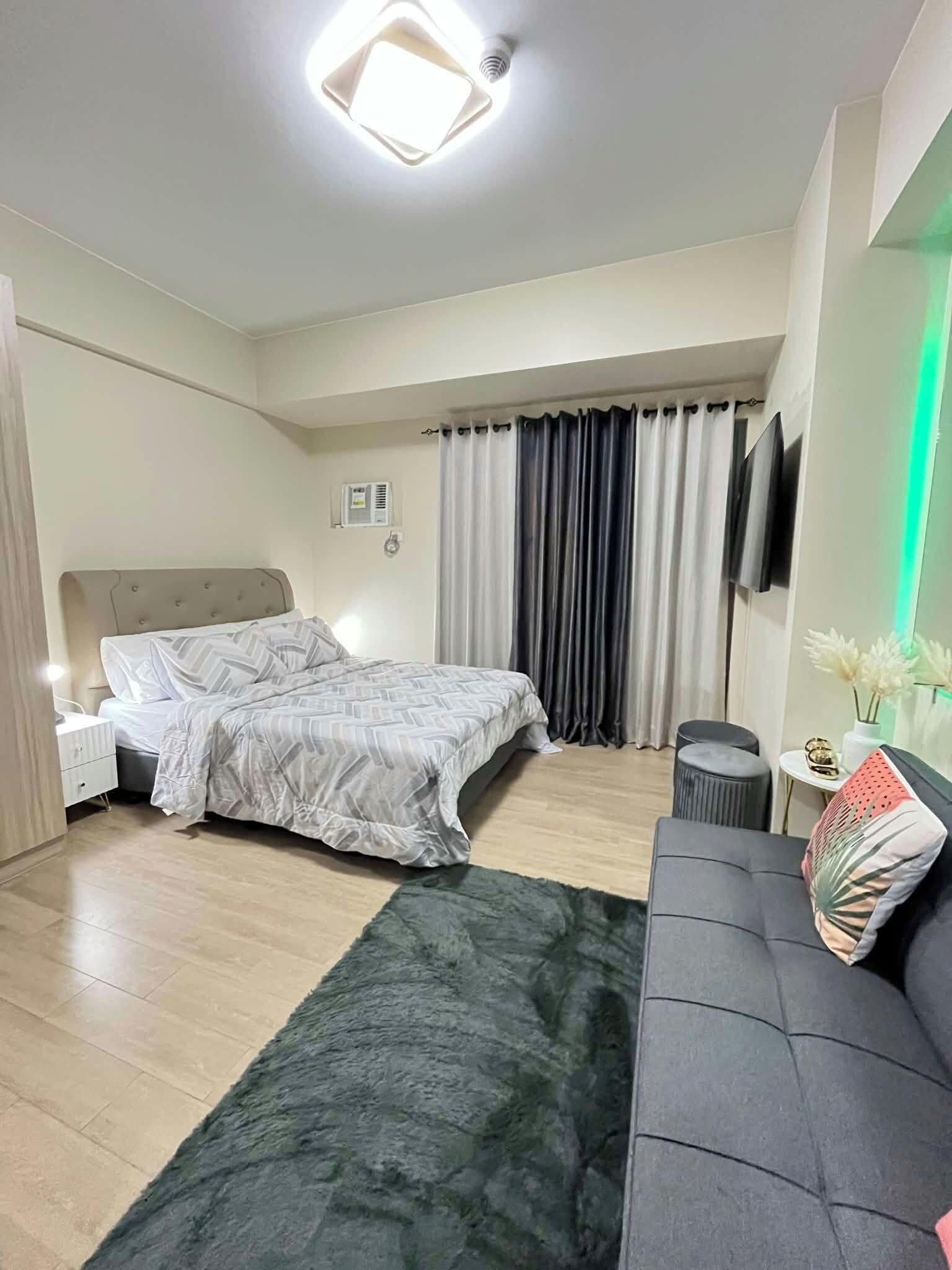 Une chambre moderne avec un lit, un canapé, une petite table ronde et un téléviseur à écran plat.