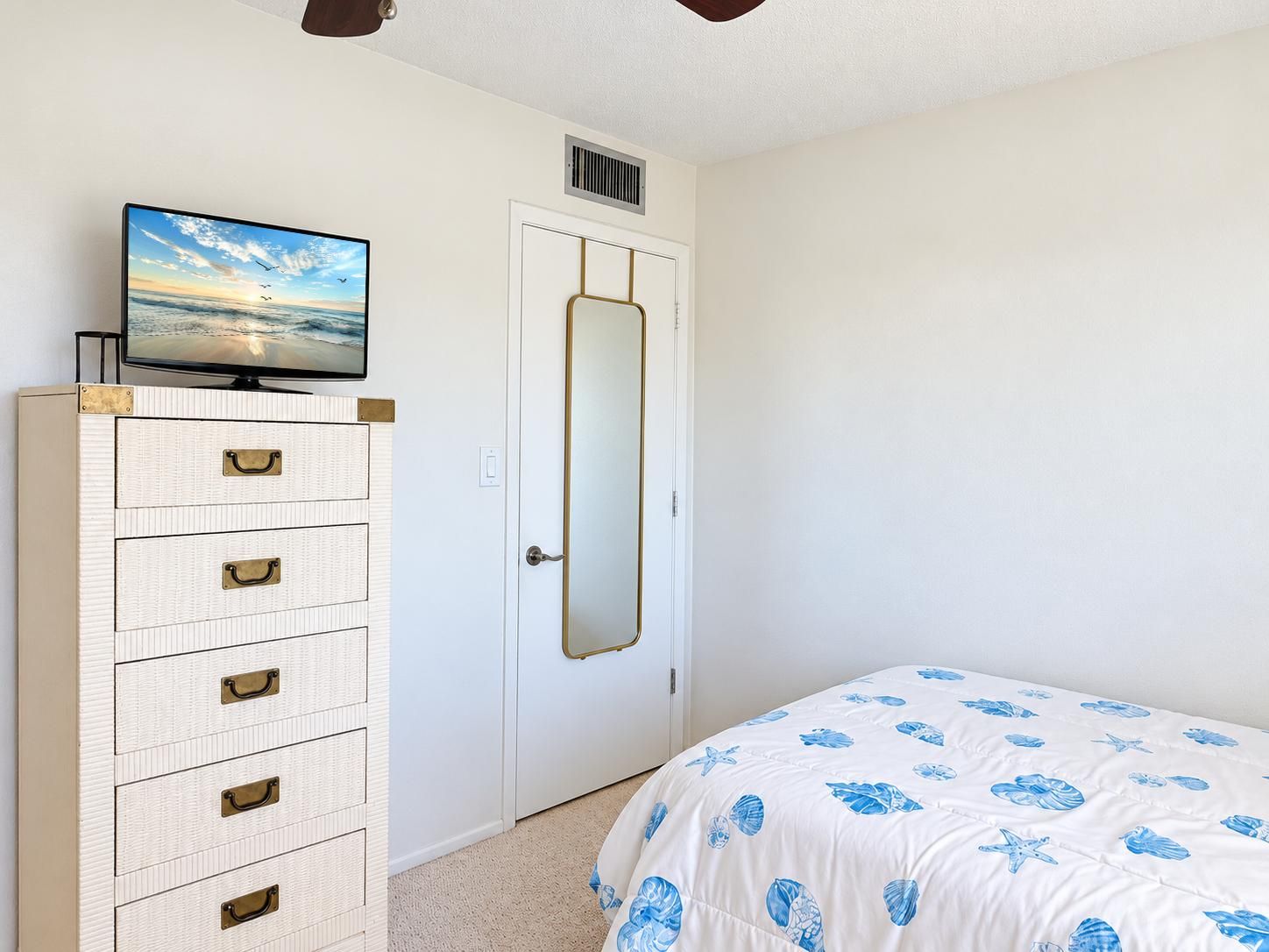 A bedroom with a bed, a dresser with drawers, a television on top, and a door with a mirror.