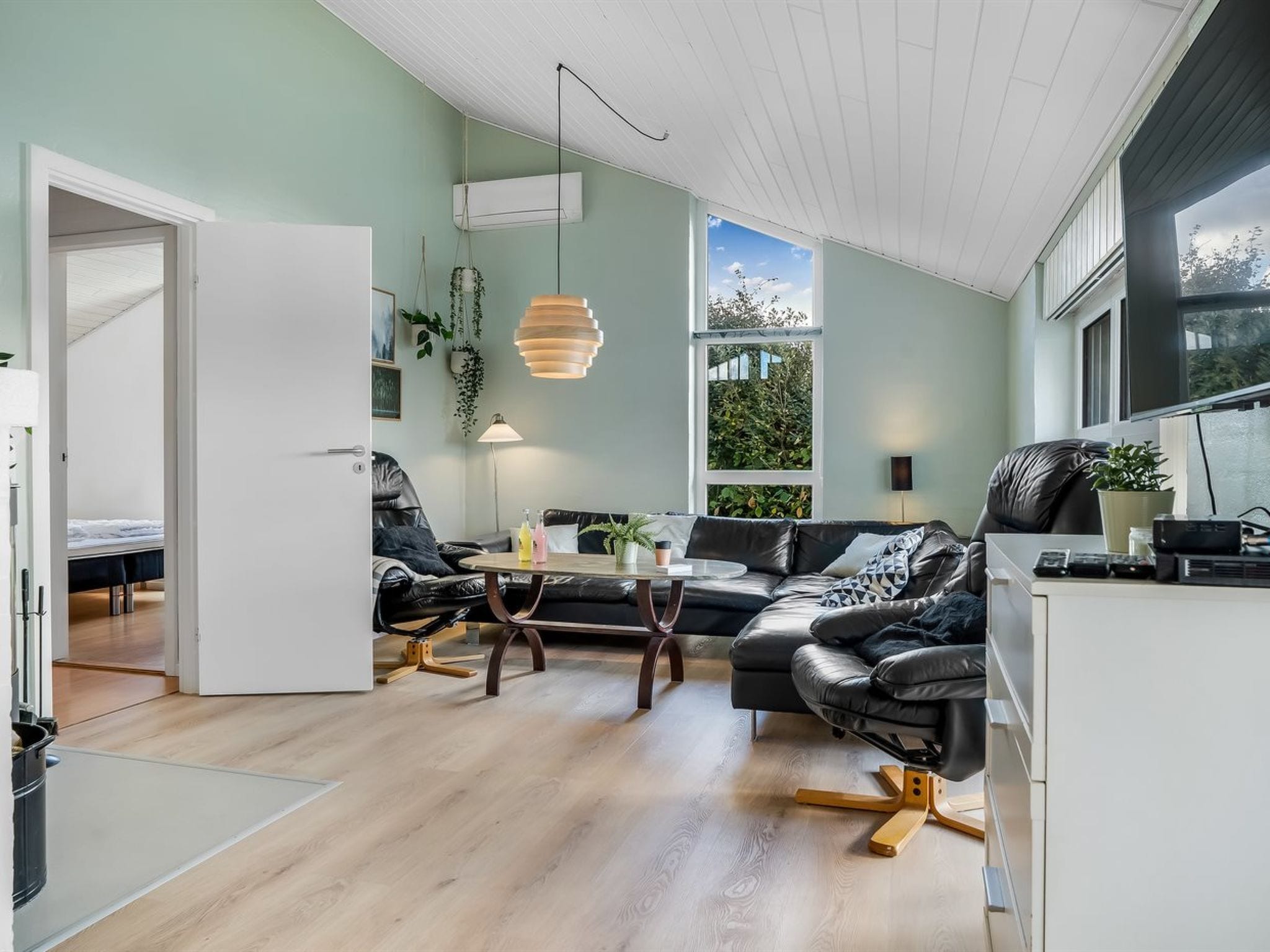 Un espacio habitable moderno con sofá, mesa de centro y zona de comedor. Hay un ventanal grande que proporciona luz natural y vistas a la vegetación exterior.