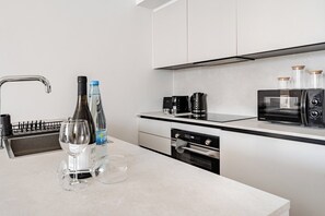 Eine moderne Küche mit Spüle aus Edelstahl, Weinflaschen, Gläsern, einer Kaffeemaschine, einem Toaster und einer Mikrowelle.