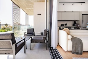 Ein stilvoller Wohnbereich mit einer Couch, Sesseln, einem Couchtisch und einem Balkon mit Glasgeländer.