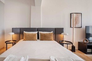 Quarto de hotel moderno com uma cama grande, duas mesas de cabeceira com luminárias, uma TV de tela plana e uma obra de arte emoldurada na parede.