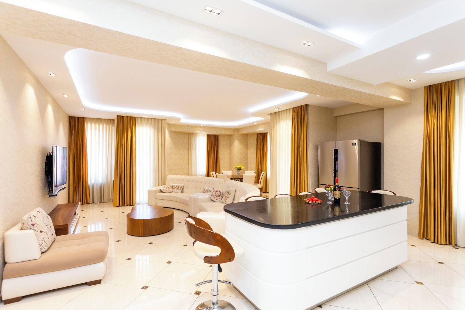 A modern living room with a sofa, a coffee table, a dining area with a table and chairs, a kitchen with a refrigerator, and a TV mounted on the wall.