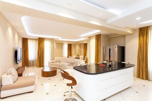 Un salon moderne comprenant un canapé, une table basse, un coin repas avec une table et des chaises, une cuisine avec un réfrigérateur et un téléviseur fixé au mur.
