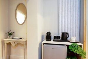 Eine kleine Küchenzeile mit Kühlschrank, Kaffeemaschine und einem Tisch mit einem Blumentopf.