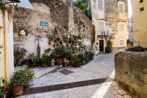 Eine schmale Gasse mit einer Steinmauer, Blumentöpfen und einem Hauseingang.