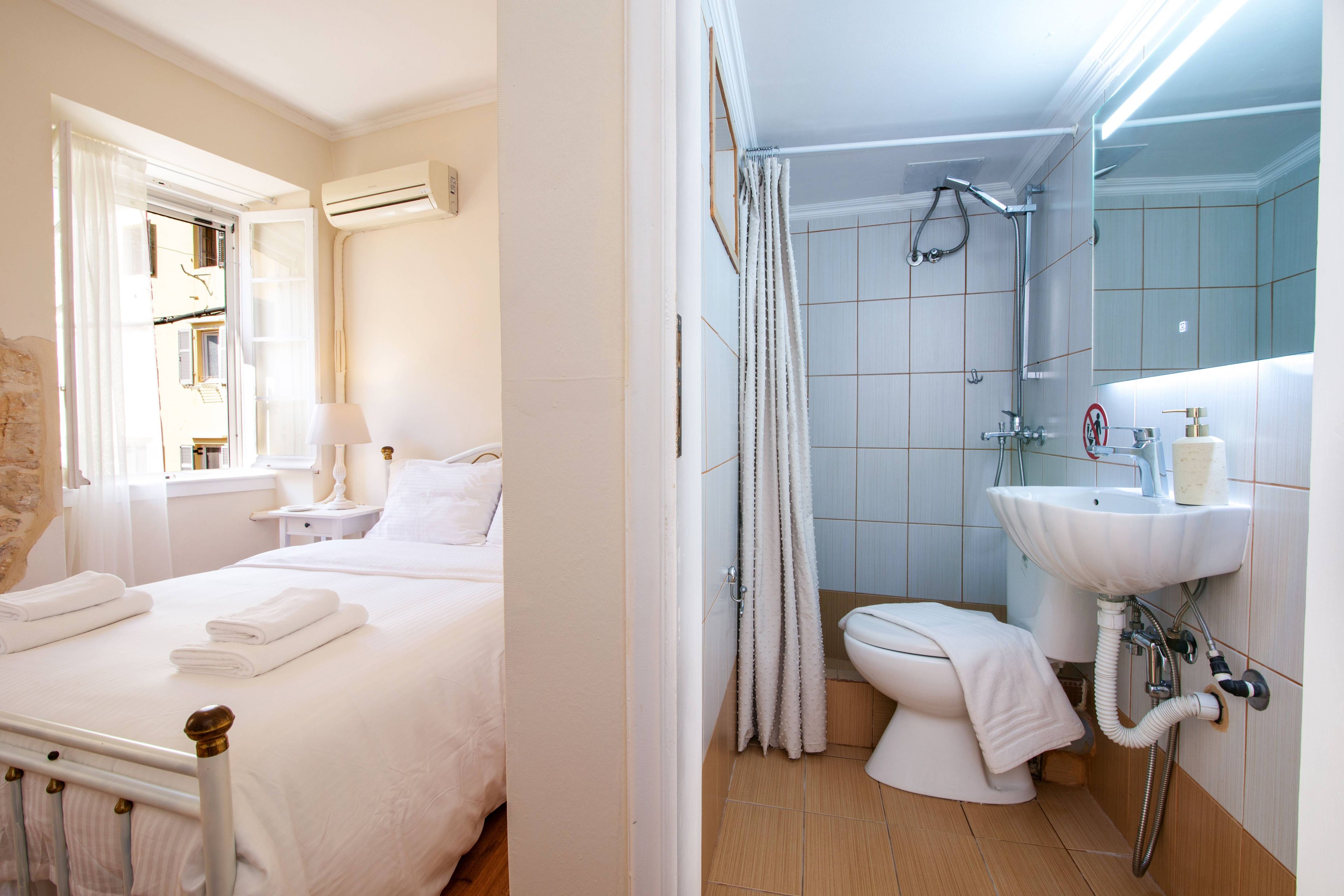 Una habitación de hotel con cama, mesita de noche, ventana con cortinas y equipo de aire acondicionado.