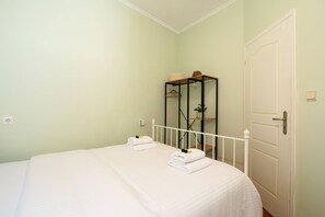 Ein Schlafzimmer mit einem Bett, einer weißen Tür, einem kleinen Regal mit Hut und Korb sowie einer Steckdose.