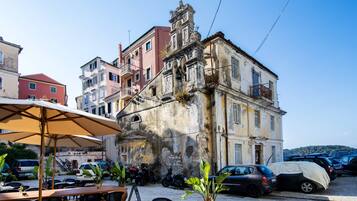 Un café al aire libre con mesas y sillas, un edificio con balcones y coches aparcados.
