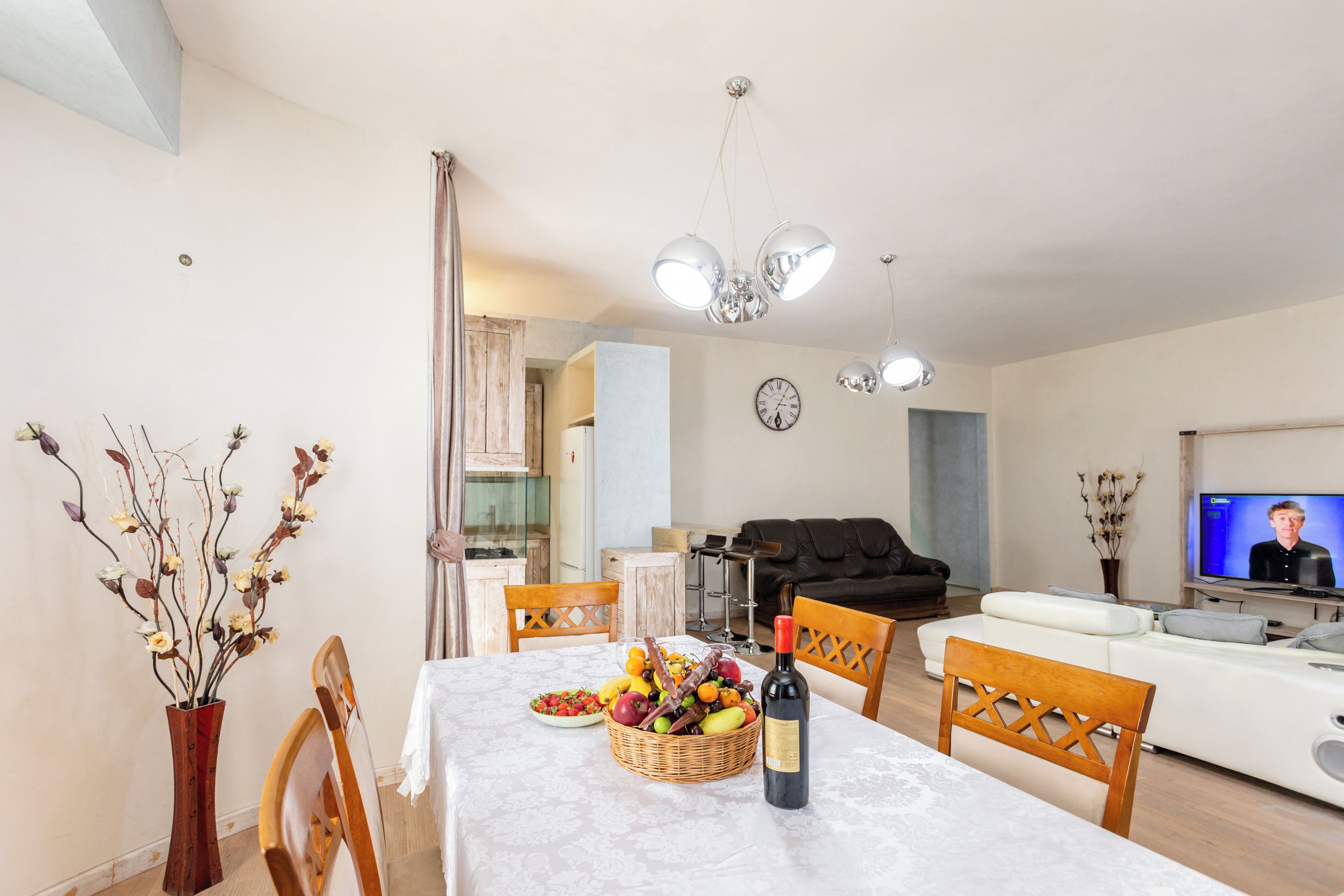 A dining area with a table set for two, a television, and a living room with a sofa and a TV screen.