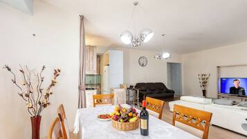 A dining area with a table set for two, a television, and a living room with a sofa and a TV screen.