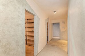 A hallway with a wooden floor, a metal shelf unit, and a door leading to a room with a light-colored wall. - Executive Central Loft (Tbilisi)