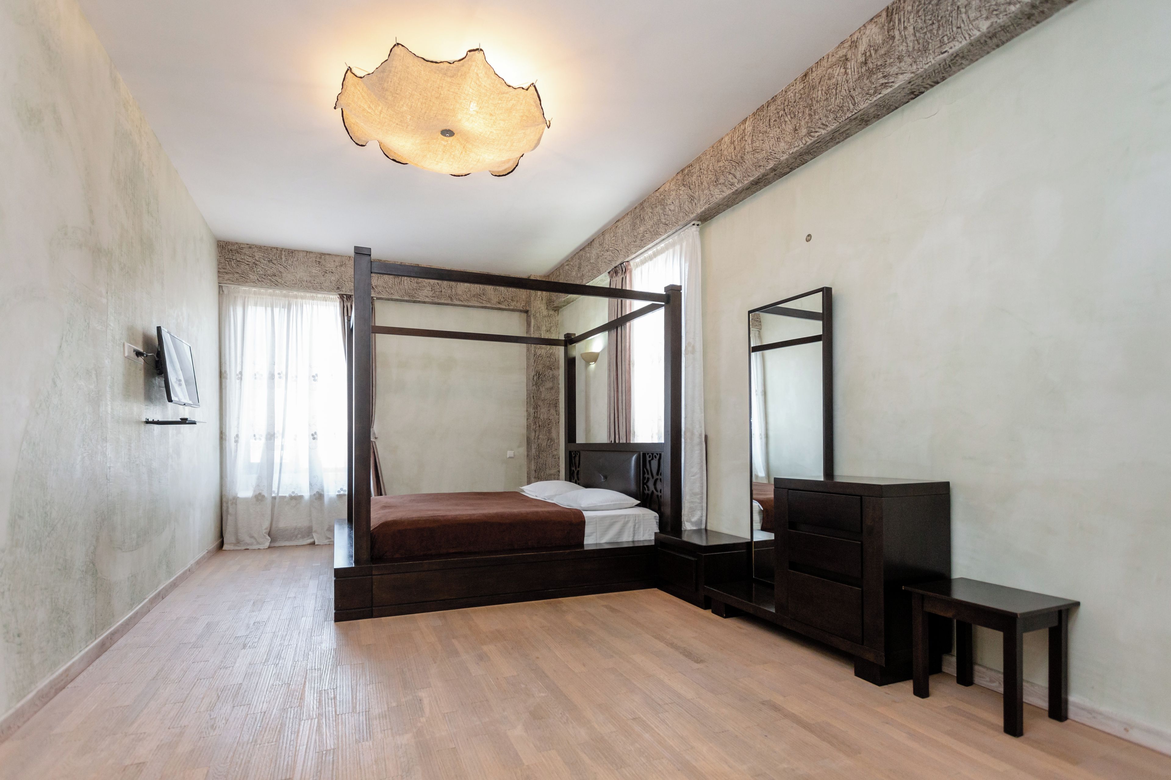 A bedroom with a four-poster bed, a bedside table, a mirror, and a television.