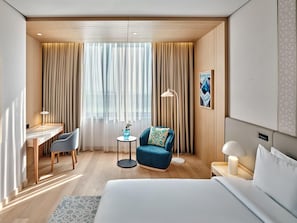 Une chambre d’hôtel avec un lit, un bureau, une chaise, une petite table, une lampe et un tableau au mur.