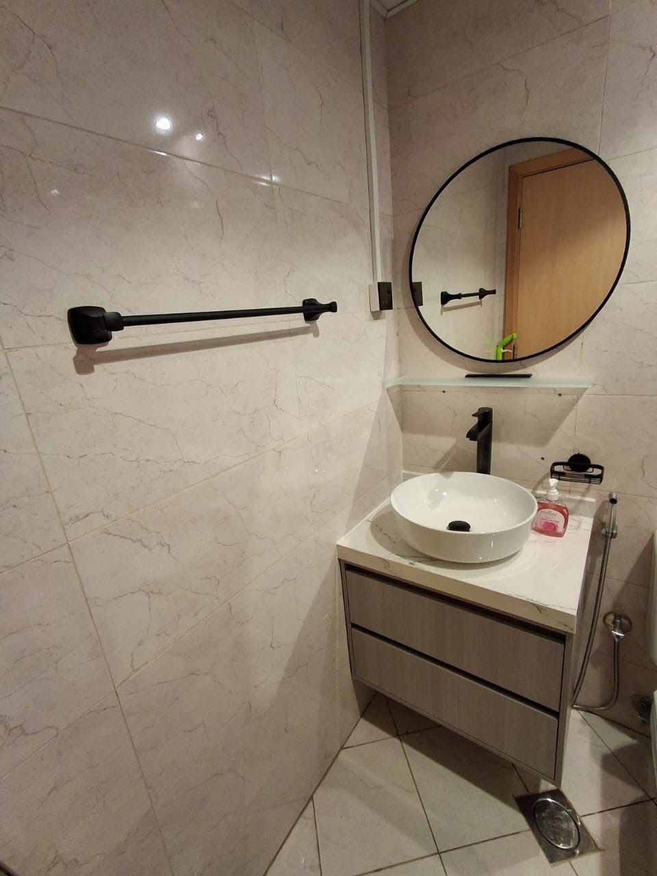 A bathroom with a white sink, a round mirror, a towel rack, and a cabinet.