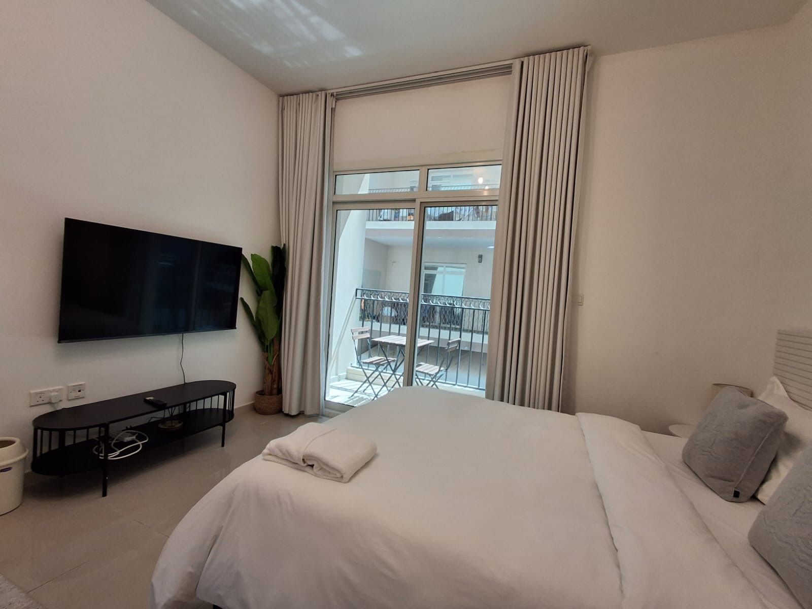 A hotel room with a bed, a TV, a small table, and a balcony with a railing.