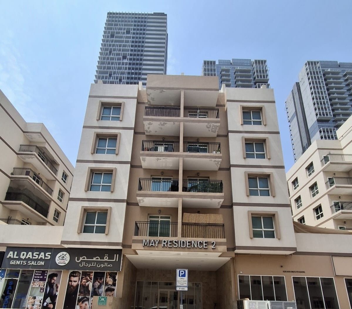 A multi-story residential building with balconies, a visible entrance, and a sign for 'MAY RESIDENCE 2'.
