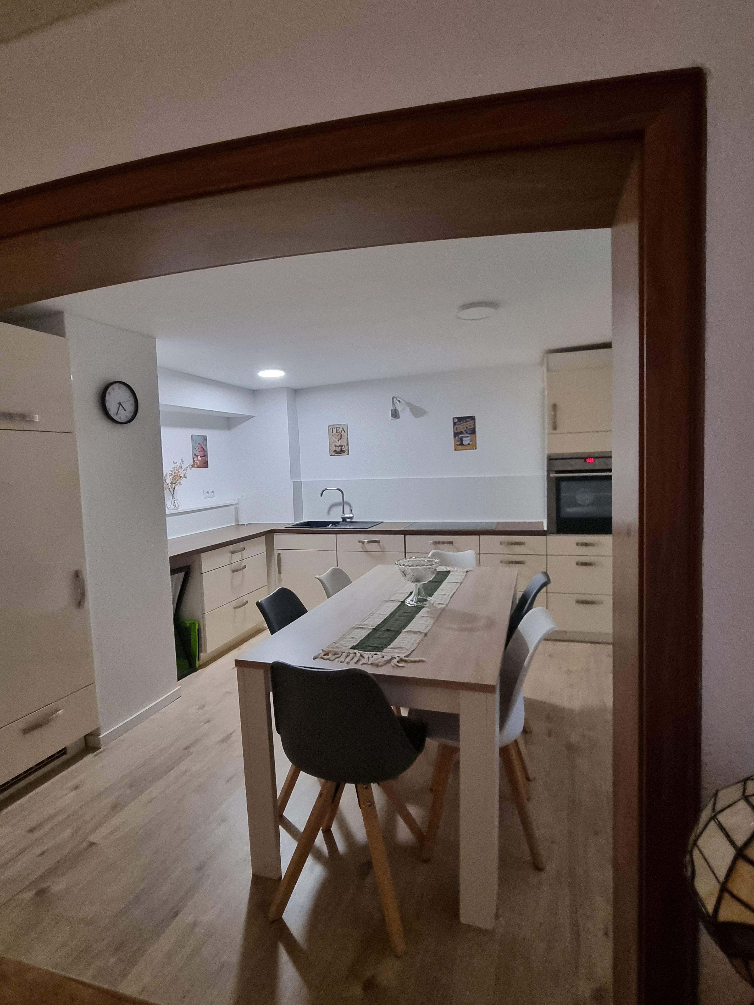 A modern kitchen with a dining area, featuring a wooden table, chairs, and a clock on the wall.