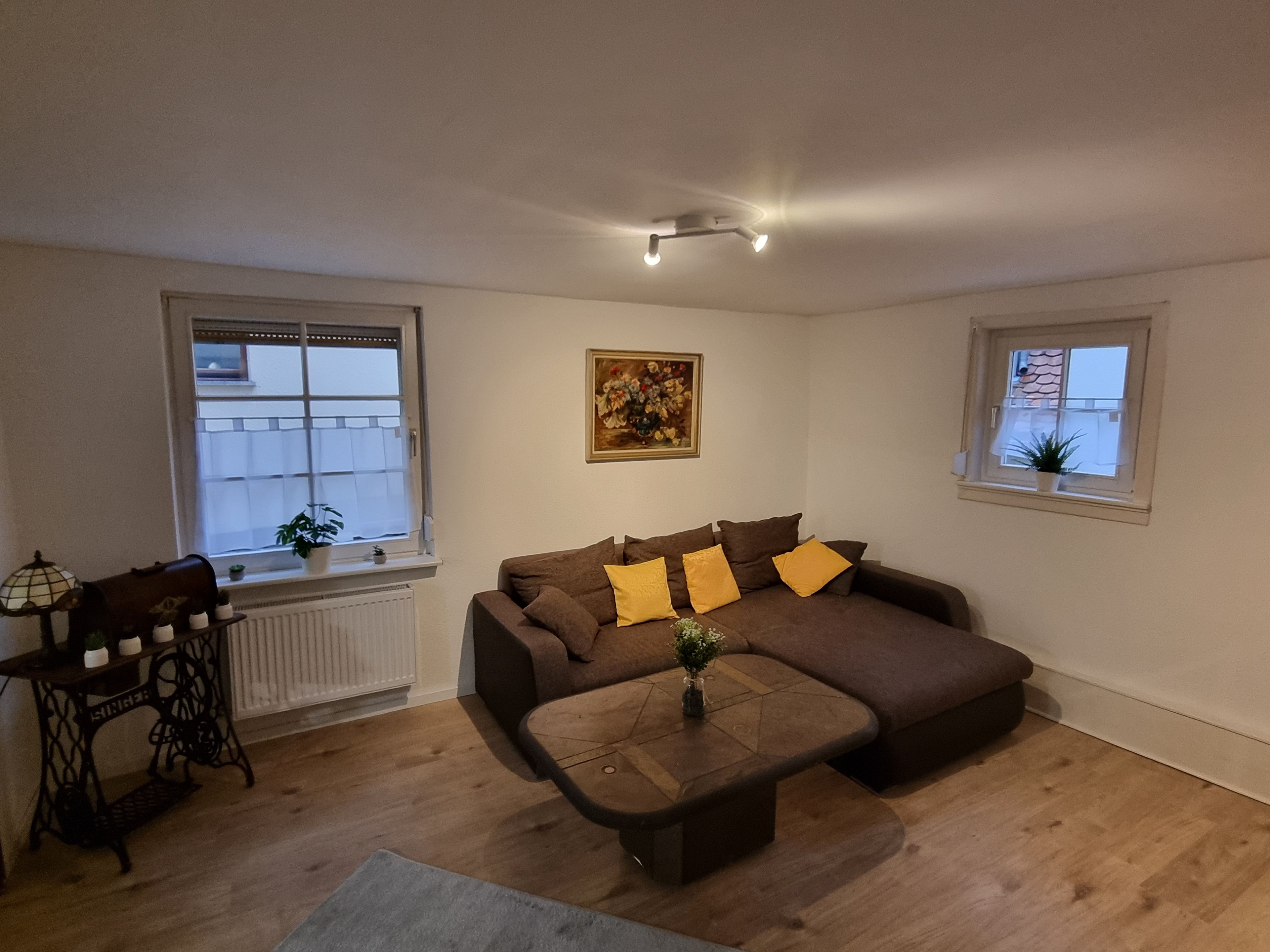 Ein Wohnzimmer mit Sofa, Couchtisch, Heizkörper, Fenster und einem Gemälde an der Wand.