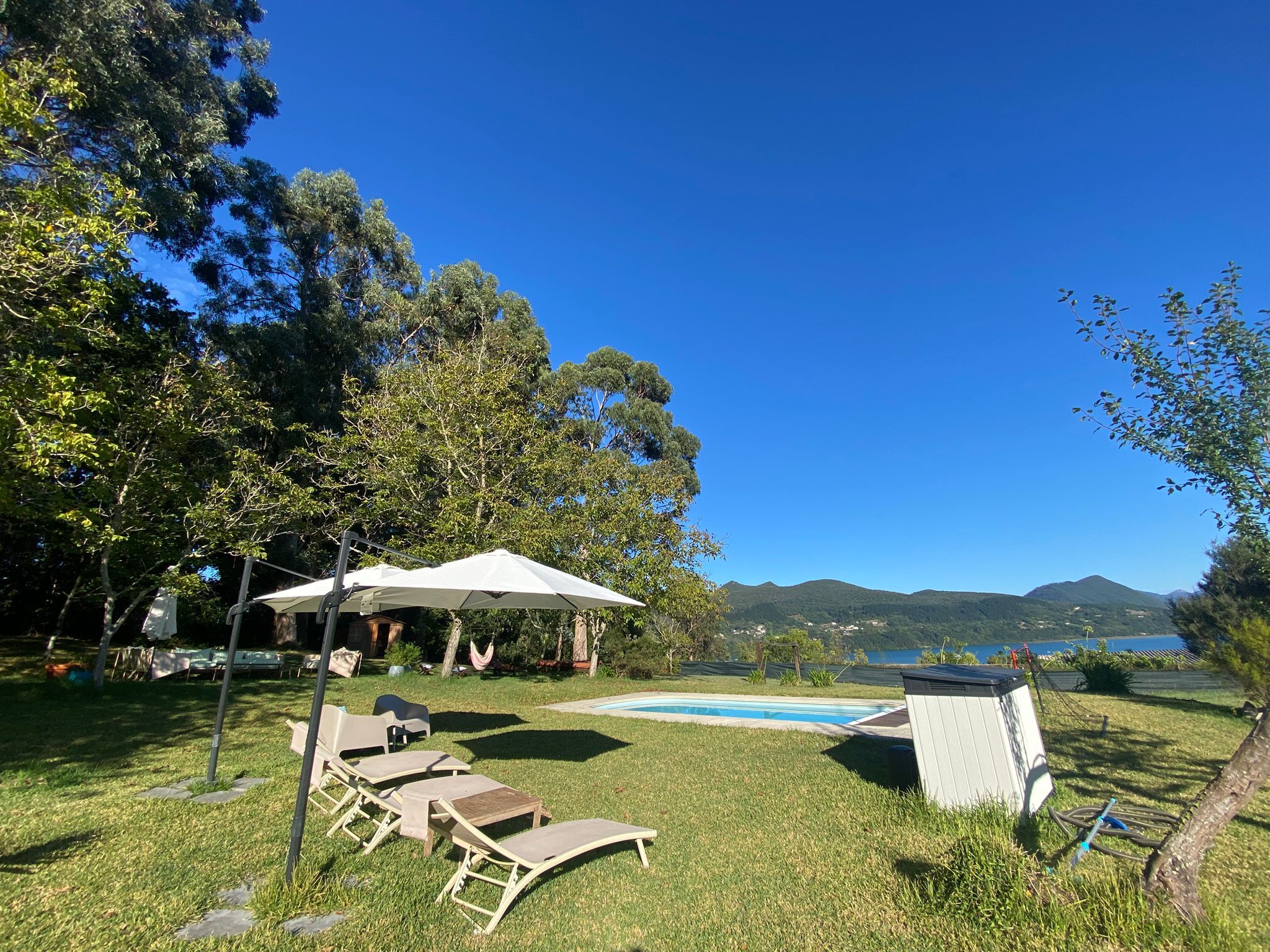 Un área junto a la piscina con sillones de descanso, una carpa y vistas a un lago y montañas.