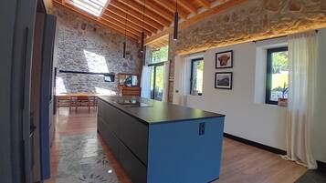 Una cocina moderna con una isla central, paredes de piedra, vigas de madera en el techo y ventanas amplias.