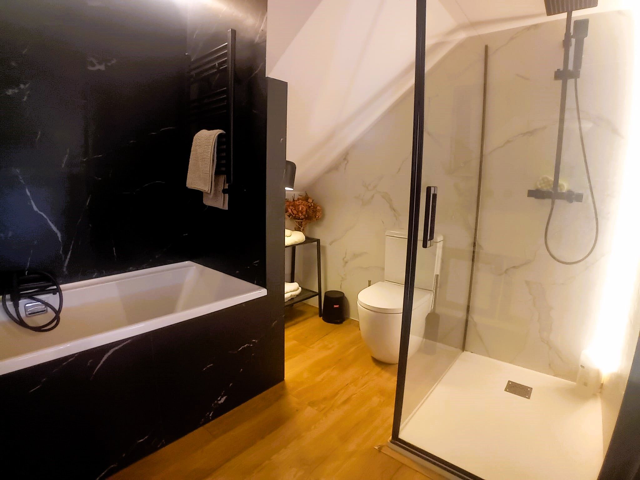 Une salle de bain moderne avec un lavabo en marbre noir, une douche à parois de verre et des toilettes blanches.