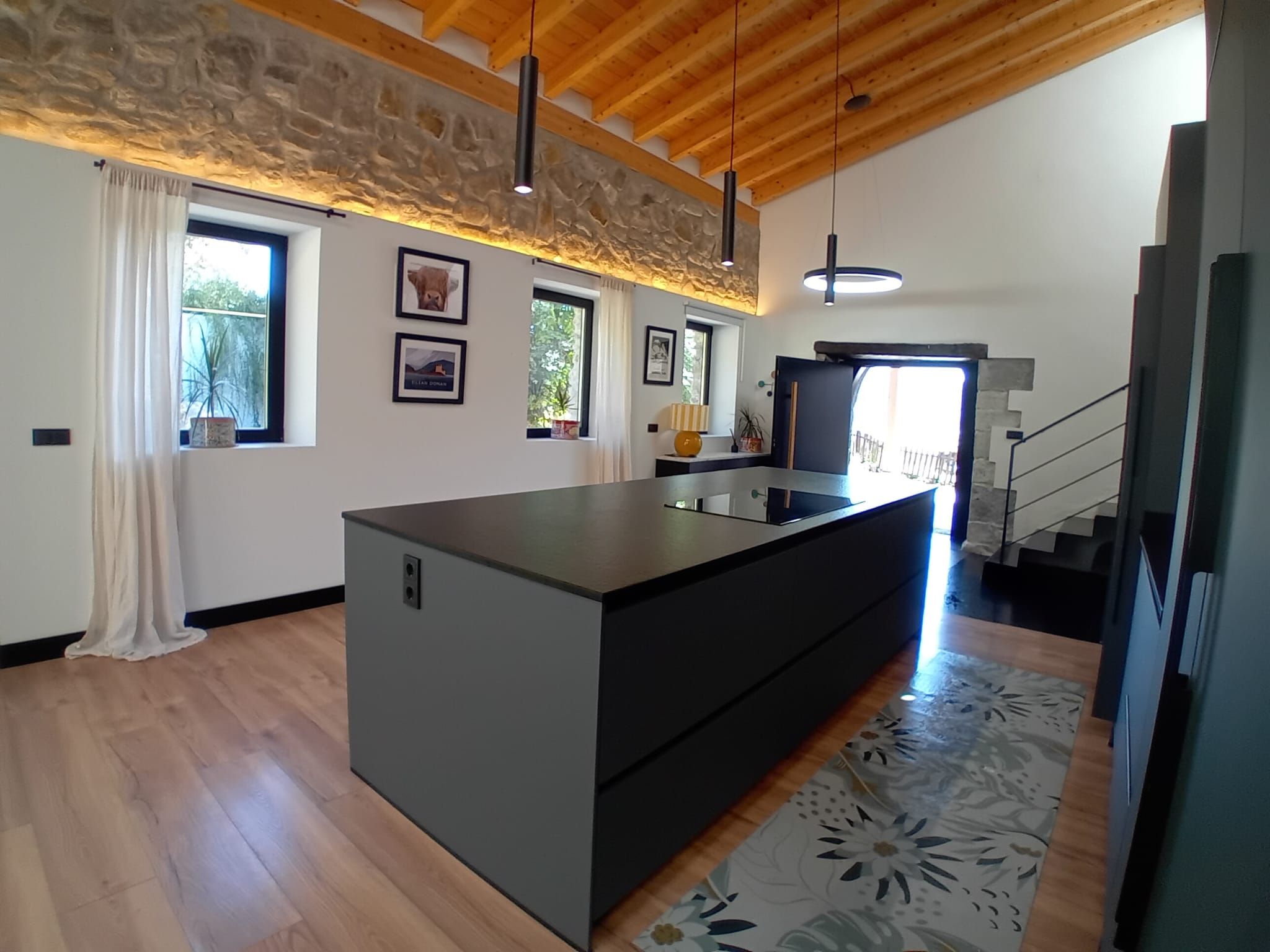 Una cocina moderna con una isla central, piso de madera e iluminación colgante.