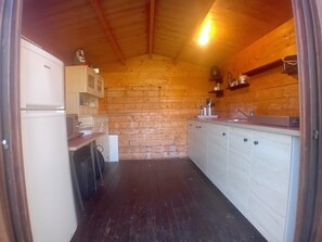 A compact kitchen with wooden walls, a refrigerator, a sink, and cabinets.