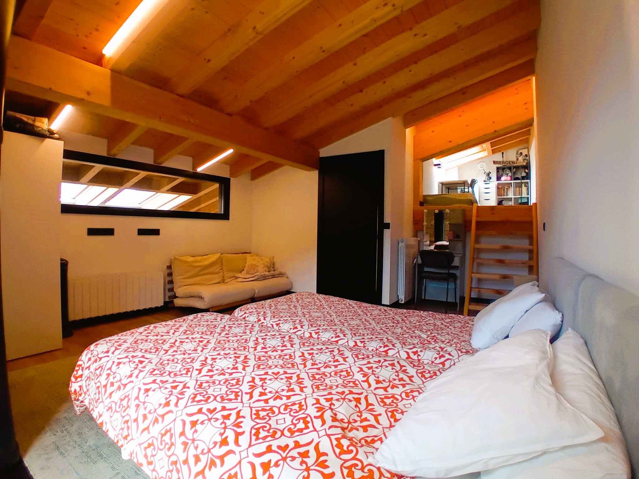 A bedroom with a large bed, a sofa, a radiator, and a mirror.