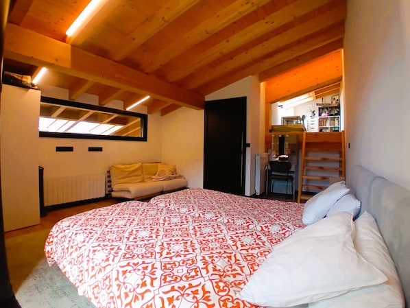 A bedroom with a large bed, a sofa, a radiator, and a mirror.