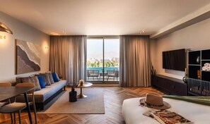 Quarto de hotel moderno com sofá, mesa de jantar e vista para uma piscina e paisagem urbana através de grandes janelas.