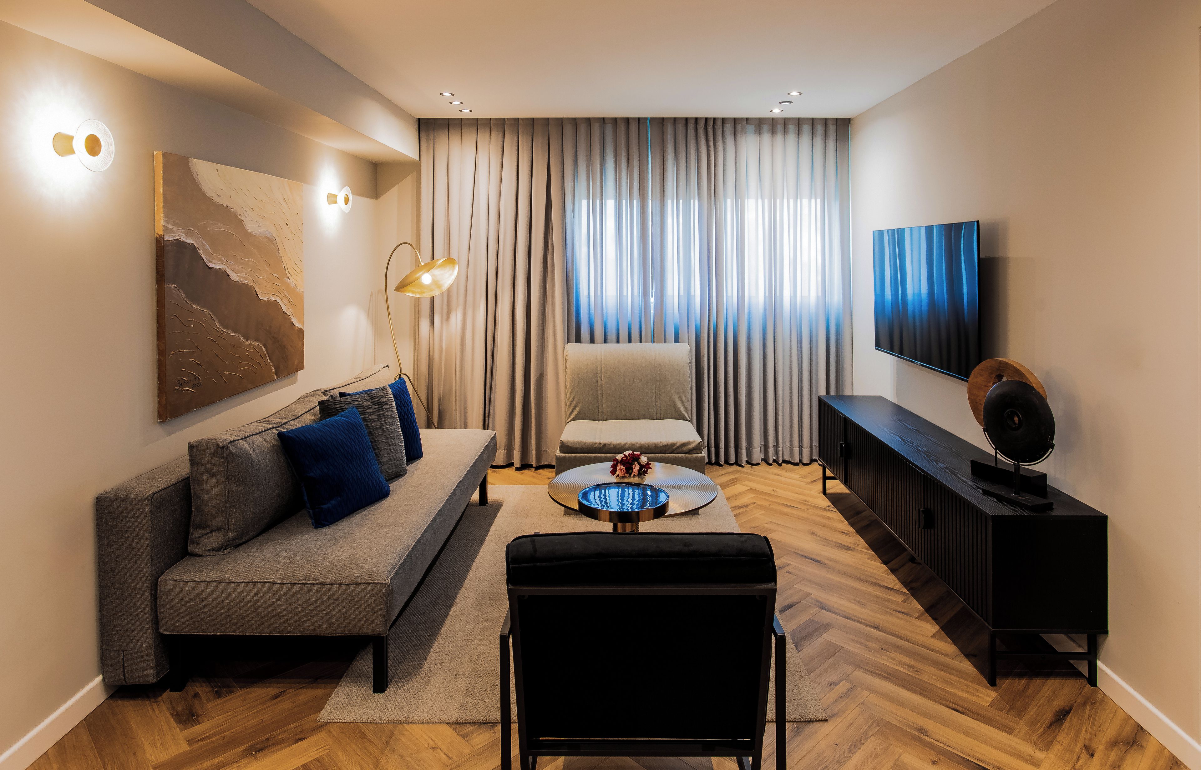 A modern living room with a sofa, ottoman, coffee table, and a flat-screen TV.
