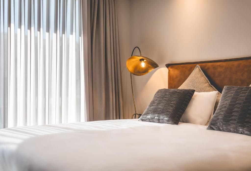 A hotel room with a bed, a lamp, and a window with curtains.