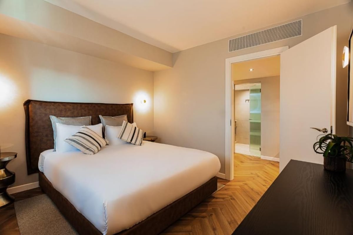 A hotel room with a large bed, bedside tables, a nightstand, a potted plant, and a view of the hallway.