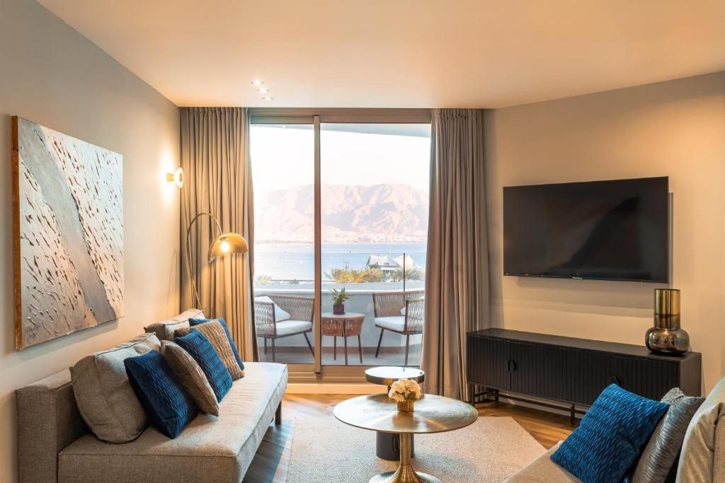 Una sala de estar moderna con un sofá, un televisor de pantalla plana, un balcón con vistas y un comedor.