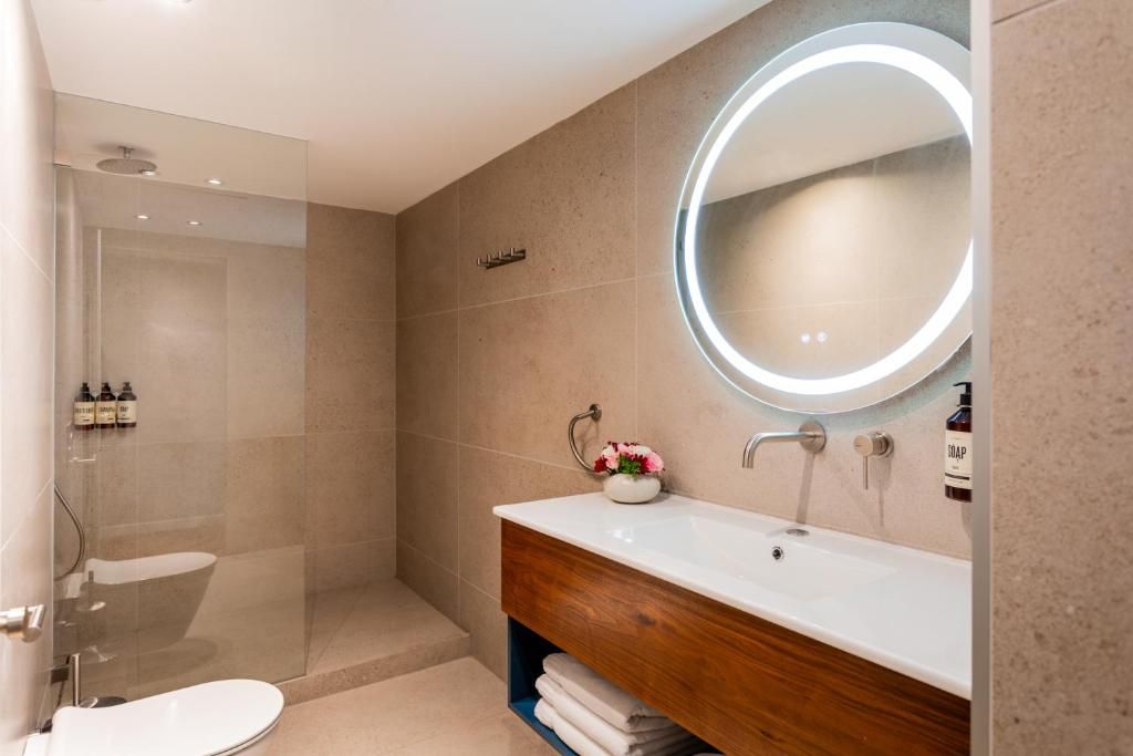 Ein modernes Badezimmer mit Glasdusche, Waschbecken mit Holzunterschrank und rundem Spiegel mit Beleuchtung.