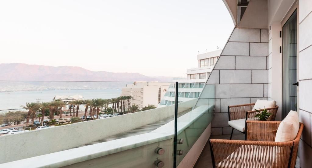 Ein Balkon mit Korbmöbeln, einer Glasreling und Blick auf Meer und Berge.