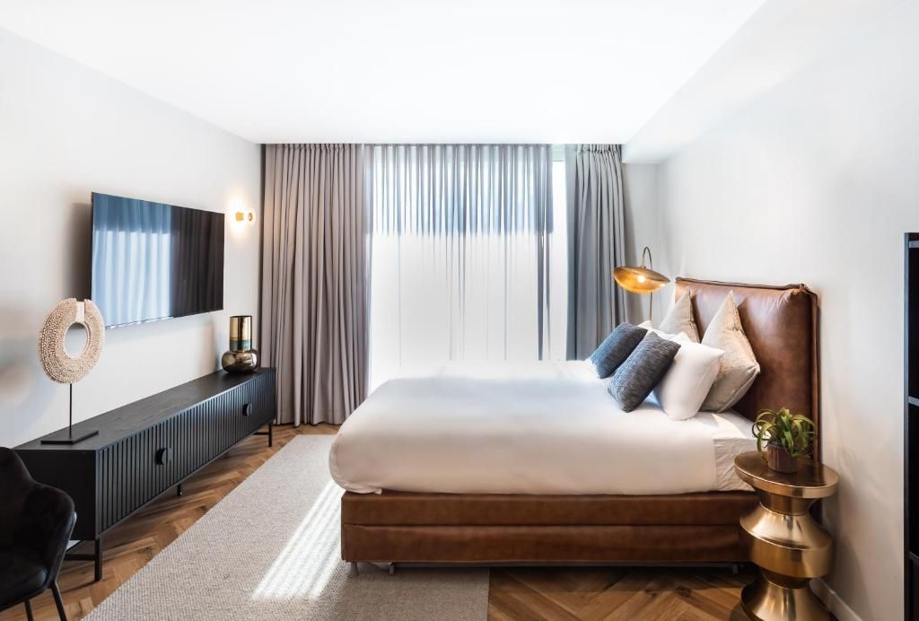 Une chambre moderne avec un grand lit, un téléviseur à écran plat, un bureau et une fenêtre avec des rideaux.