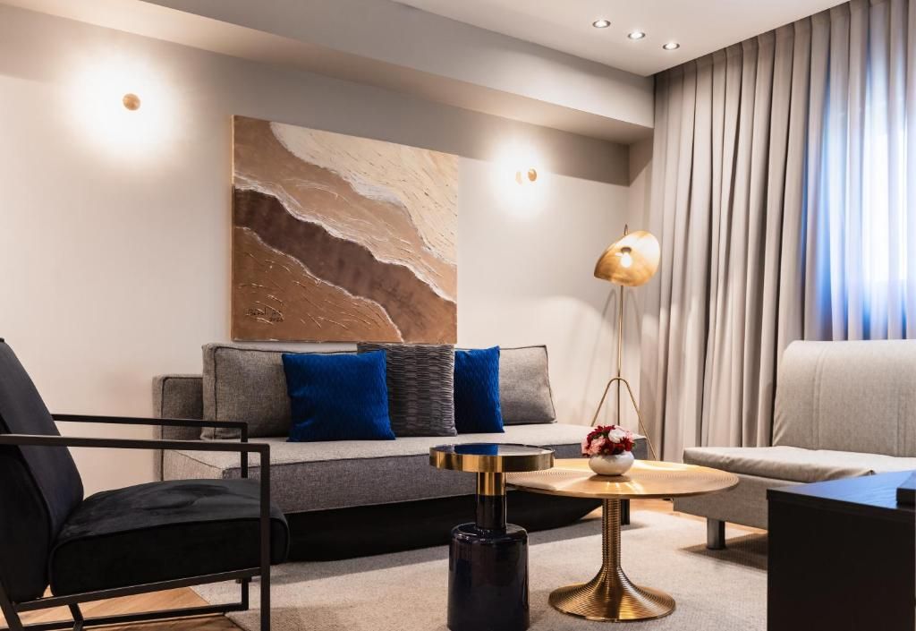 Un salon moderne avec un canapé, des fauteuils, une table basse et un grand tableau abstrait accroché au mur.