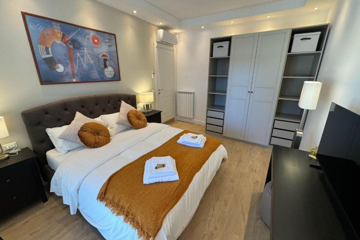 Ein Hotelzimmer mit Bett, Nachttischen, Schreibtisch, Fernseher, Kleiderschrank und einem Bild an der Wand.