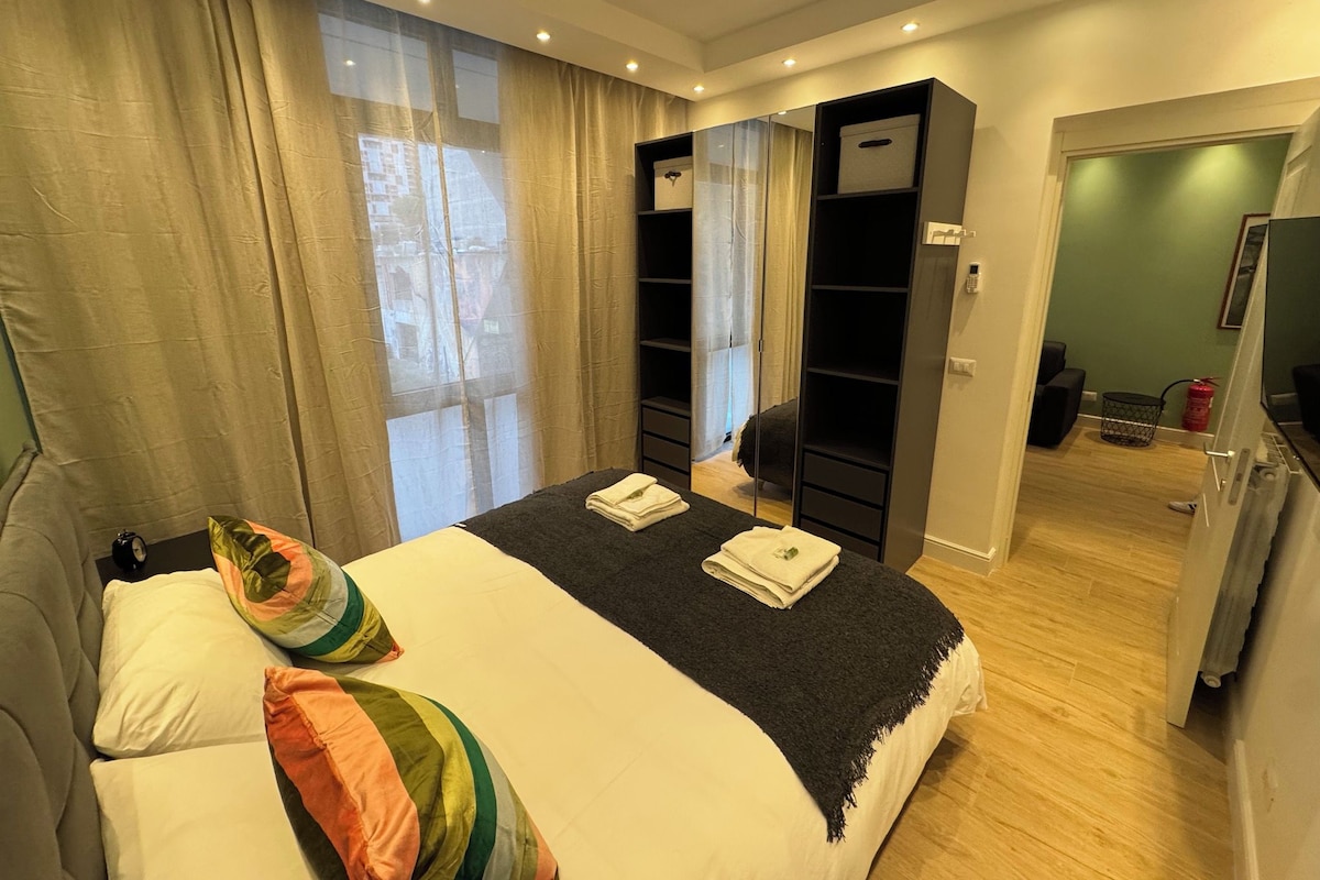 Ein modernes Schlafzimmer mit einem großen Bett, einem Kleiderschrank und einer Tür zu einem weiteren Zimmer.