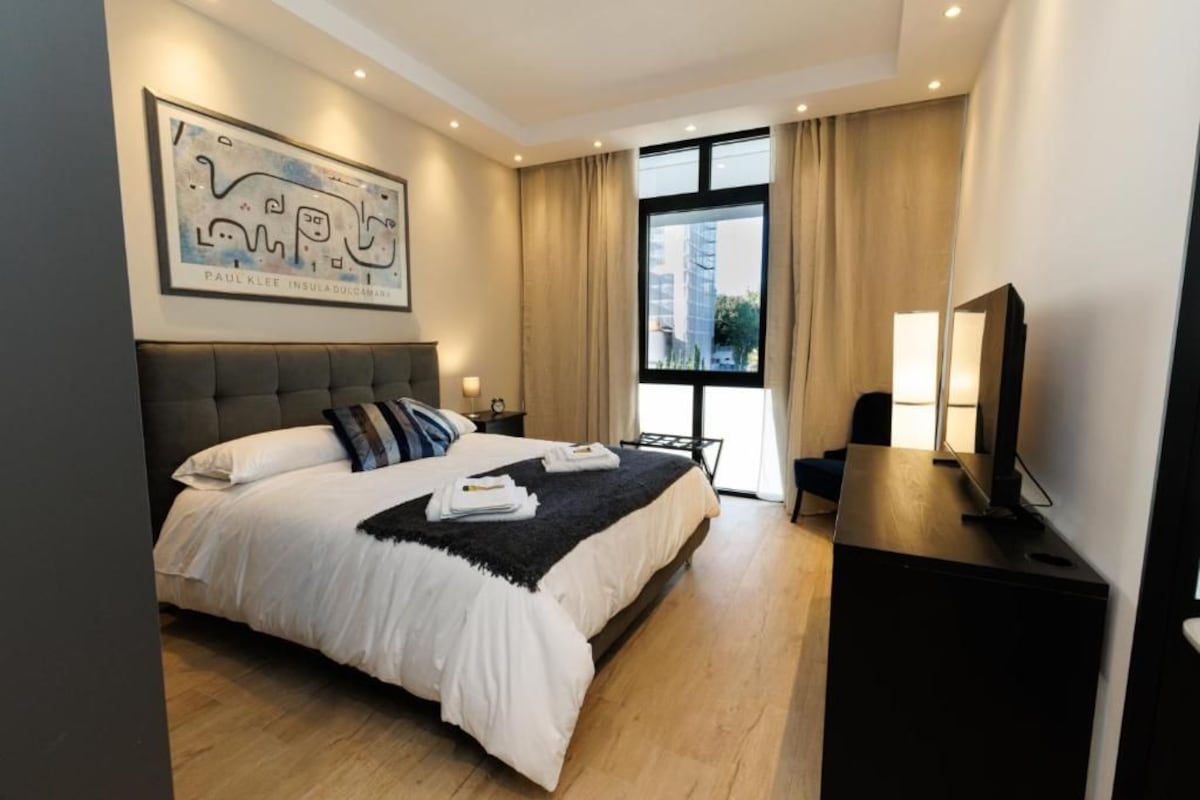 Ein modernes Hotelzimmer mit einem großen Bett, einem Schreibtisch, einem Fernseher und einem fenster mit Vorhängen.