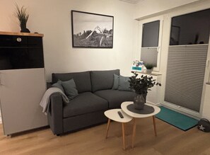 A living room with a grey sofa, a small round table with a vase, a black and white framed picture on the wall, and a sliding glass door. - New Listing (Winterberg)