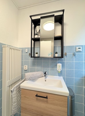 A bathroom with a white sink, a towel, a wooden cabinet, a mirror, and a radiator. - New Listing (Winterberg)