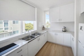 Een moderne keuken met witte kastjes, een roestvrijstalen spoelbak en een waterkoker op het aanrecht.
