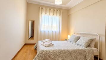 A bedroom with a bed, a bedside table, a lamp, a mirror, and a window with curtains.