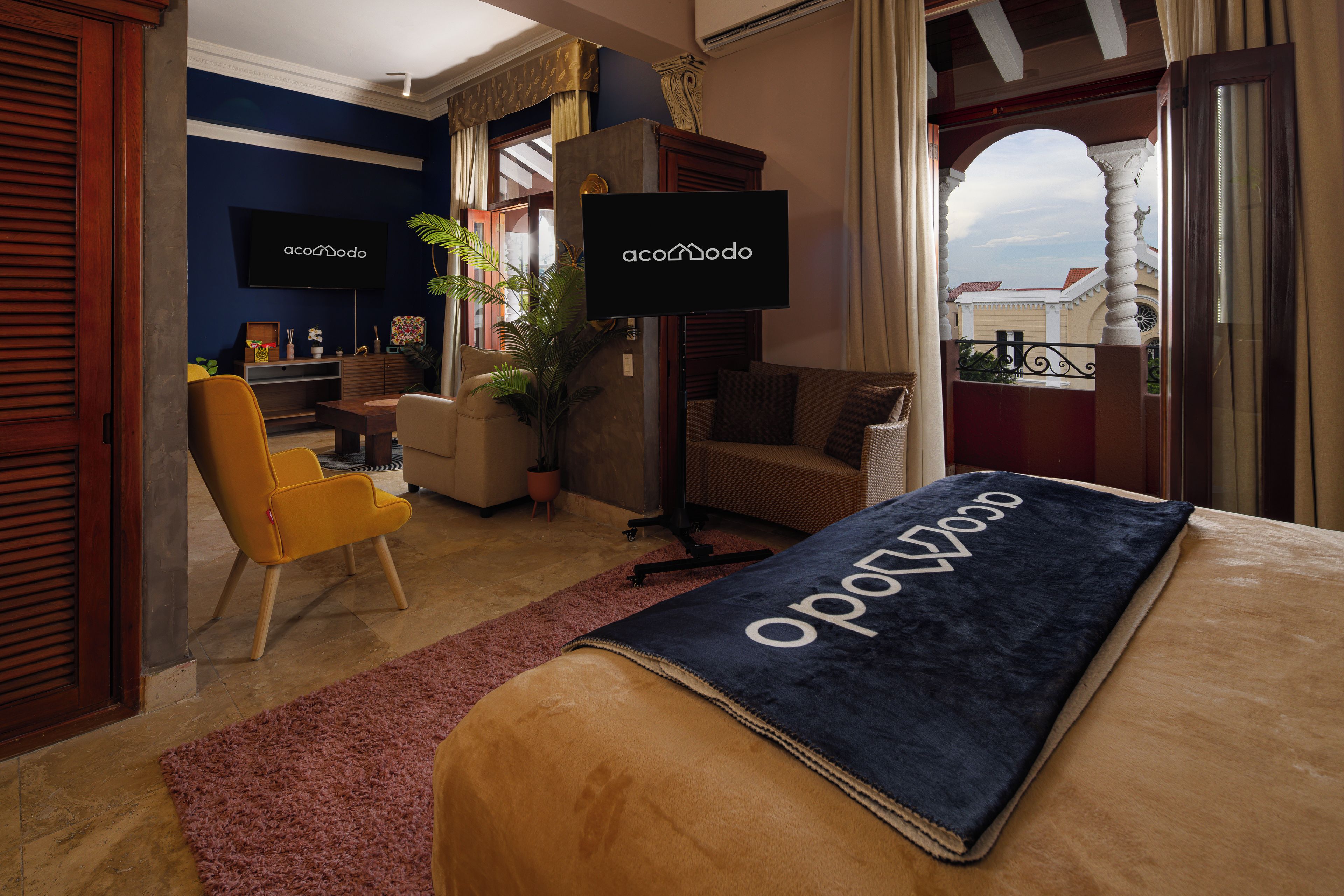 Habitación de hotel con cama, sofá, sillón, televisi ón y balcón con vistas.