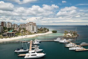A marina with multiple yachts docked, a beach, and high-rise buildings in the background.